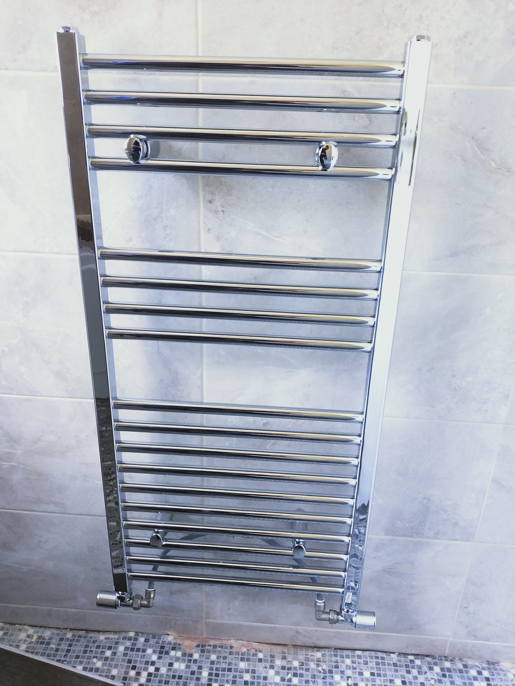 Tall chrome ladder towel radiator fitted on marble-effect tiles